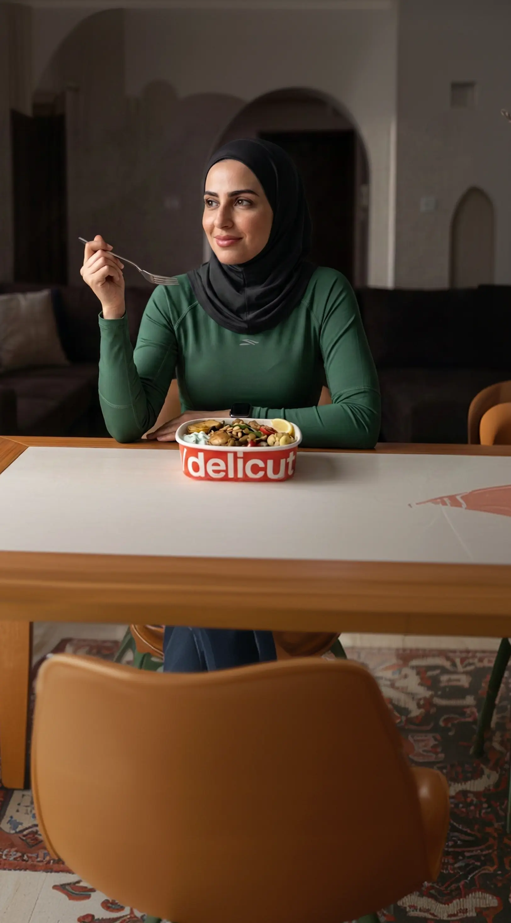امرأة بعباءة خضراء تستمتع بطبق عربي من ديليكت في منزلها